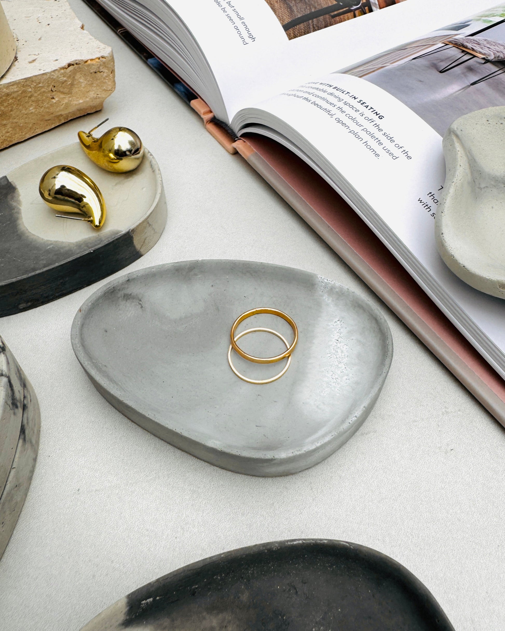 Gray and black ceramic trinket dishes with gold jewelry on a surface with an open book.